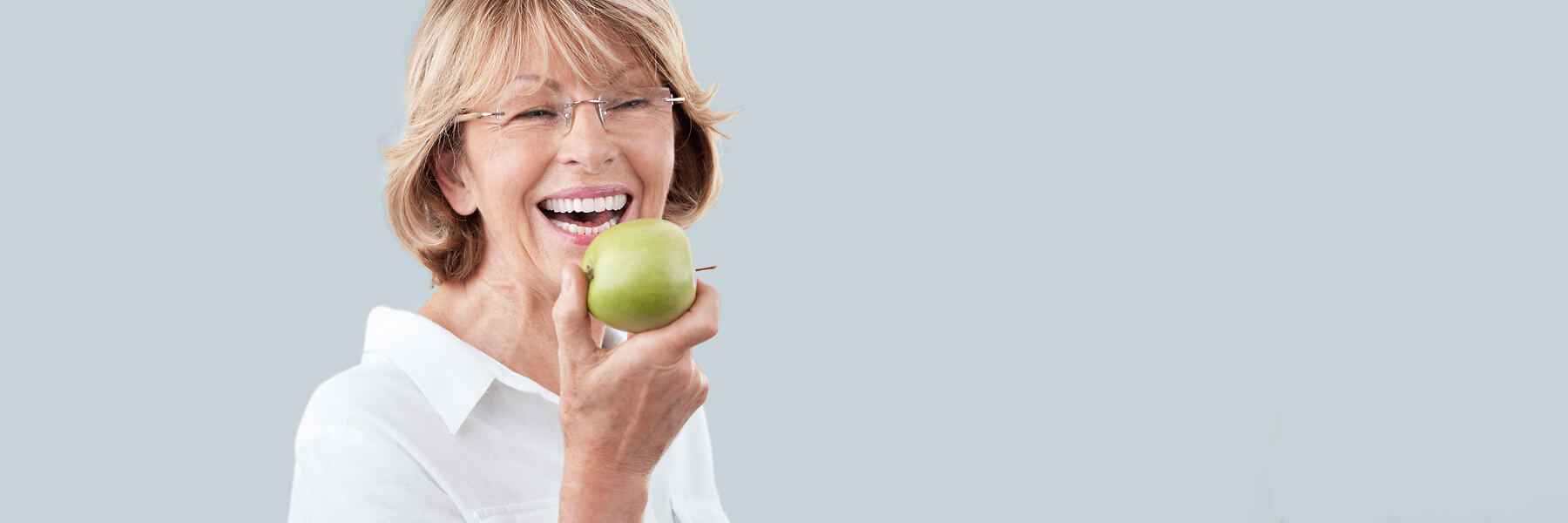 Seniorin lächelt mit einem Apfel im Hand